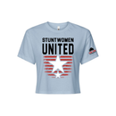Stuntwomen United light blue women’s cropped T-shirt shown from the front, featuring bold STUNTWOMEN UNITED text with distressed red stripe star graphic and Stunt Team sleeve logo.