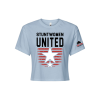 Stuntwomen United light blue women’s cropped T-shirt shown from the front, featuring bold STUNTWOMEN UNITED text with distressed red stripe star graphic and Stunt Team sleeve logo.