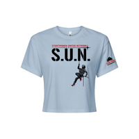 Stuntwomen United light blue women’s cropped T-shirt shown from the front, featuring S.U.N. logo with rappelling stuntwoman graphic in red heels and Stunt Team sleeve logo.
