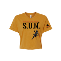 Stuntwomen United mustard yellow women’s cropped T-shirt shown from the front, featuring S.U.N. logo with rappelling stuntwoman graphic in red heels and Stunt Team sleeve logo.