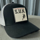 Close-up of a black and white Stuntwomen United Network Richardson trucker hat featuring a velcro-backed rubber patch on the front panel.