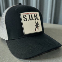 Close-up of a black and white Stuntwomen United Network Richardson trucker hat featuring a velcro-backed rubber patch on the front panel.