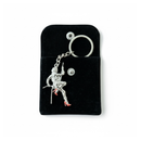 Stuntwomen United metal keychain featuring a stuntwoman rappelling figure with red heels, displayed on a black pouch.