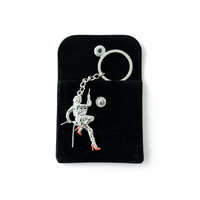 Stuntwomen United metal keychain featuring a stuntwoman rappelling figure with red heels, displayed on a black pouch.